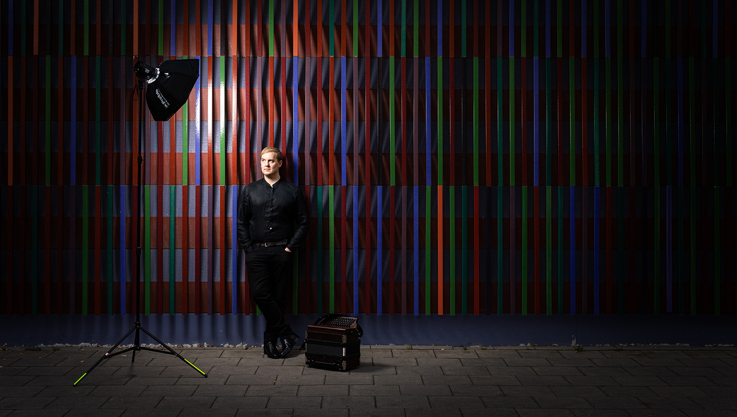 Matthias Puerner standing behind a colorful wall in the dark, only lit by one spotlight